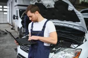 car mechanic using a computer laptop to diagnosing and checking up on car engines parts for fixing and repair photo