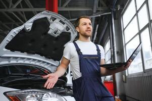 car mechanic using a computer laptop to diagnosing and checking up on car engines parts for fixing and repair photo
