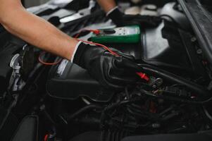 Car mechanic is using a multimeter with voltage range measurement to check the voltage level of the car battery. photo