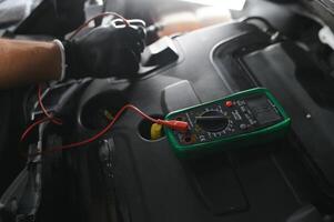 Car mechanic is using a multimeter with voltage range measurement to check the voltage level of the car battery. photo