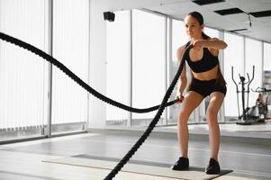 Athletic Female in a Gym Exercises with Battle Ropes During Her Fitness Workout High-Intensity Interval Training. She's Muscular and Sweaty photo
