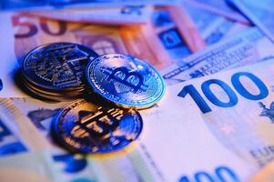 Close up heap of golden bitcoin physical coins on top of Euro, dollar banknotes background, high angle view, selective focus photo