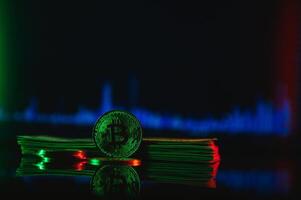 Golden bitcoin are stacked on a bright background of business graphs close-up. Bitcoin cryptocurrency. Folded in a tube 100 dollar bills photo