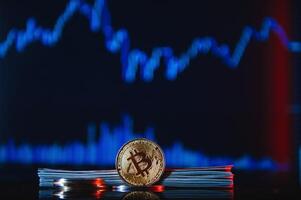 Golden bitcoin are stacked on a bright background of business graphs close-up. Bitcoin cryptocurrency. Folded in a tube 100 dollar bills photo