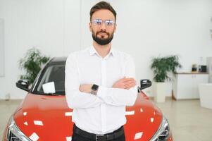Happy young guy checking new luxury car, buying automobile at dealership centre. Portrait of cheerful millennial Caucasian man examining auto at showroom store photo