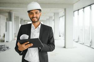 Confident asian engineer man Using tablet for checking and maintenance to inspection at modern home building construction. Architect working with white safety helmet in construction site. photo