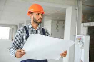 indio masculino construcción trabajador en pie en uniforme y difícil sombrero a construcción sitio. foto