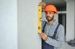 Indian construction site manager standing wearing helmet, thinking at construction site. Portrait of mixed race manual worker or architect. photo