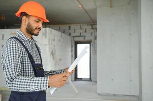 indio masculino construcción trabajador en pie en uniforme y difícil sombrero a construcción sitio. foto