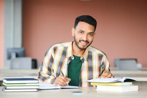 Young indian student boy reading book studying in college library with bookshelf behind. working on assignment or project photo