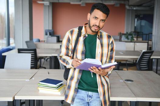 Young indian student boy reading book studying in college library with bookshelf behind. working on assignment or project photo