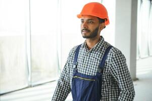 indio masculino construcción trabajador en pie en uniforme y difícil sombrero a construcción sitio. foto
