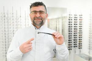Handsome ophthalmologist holding eyeglasses for a try out. Optometrist offering to wear a pair of glasses. Image with small deph of field focused on the hands and glasses photo