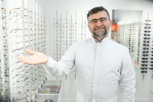Portrait of a handsome ophthalmologist in front of the showcase with eyeglasses in the hospital. photo