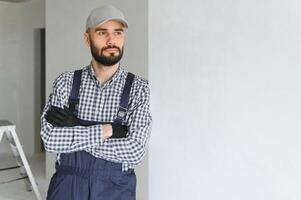 Portrait of handsome mechanic with stubble in blue overall, shirt having his arms crossed, looking at camera photo