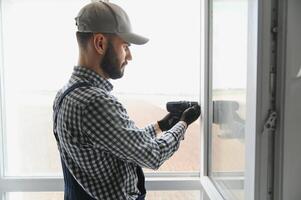 Workman in overalls installing or adjusting plastic windows in the living room at home photo