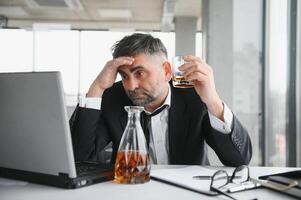 Old male employee drinking alcohol at workplace photo