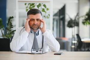 Senior caucasian man wearing doctor uniform and stethoscope at the clinic rubbing eyes for fatigue and headache, sleepy and tired expression. vision problem photo