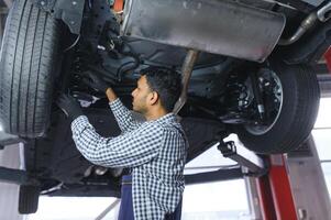 latin hispanic auto mechanic in uniform is examining a car while working in auto service photo