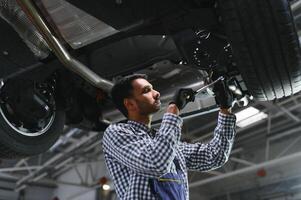 latin hispanic auto mechanic in uniform is examining a car while working in auto service photo