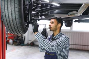latin hispanic auto mechanic in uniform is examining a car while working in auto service photo