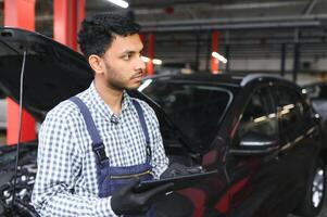 Mechanic man mechanic manager worker using a laptop computer checking car in workshop at auto car repair service center. Engineer young man looking at inspection vehicle details under car hood. photo