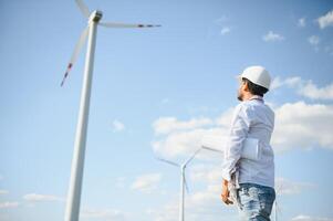 Engineer India man working at windmill farm Generating electricity clean energy. Wind turbine farm generator by alternative green energy. Asian engineer checking control electric power photo