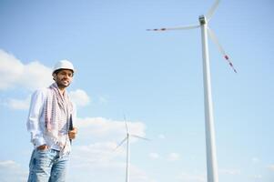 Engineer India man working at windmill farm Generating electricity clean energy. Wind turbine farm generator by alternative green energy. Asian engineer checking control electric power photo