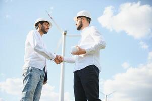 Two engineers discussing against turbines on wind turbine farm. photo