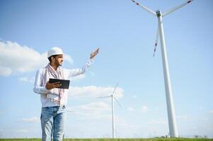 Engineer India man working at windmill farm Generating electricity clean energy. Wind turbine farm generator by alternative green energy. Asian engineer checking control electric power photo