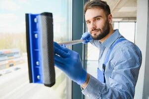 Male professional cleaning service worker in overalls cleans the windows and shop windows of a store with special equipment photo