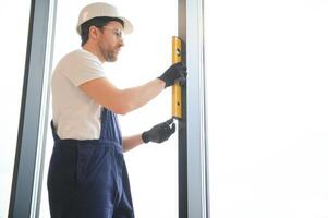Worker using bubble level after plastic window installation indoors photo
