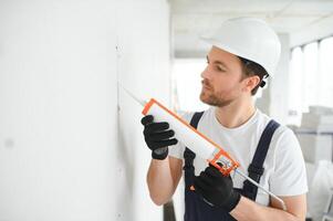 Professional Workman Applying Silicone Sealant With Caulking Gun on the Wall photo