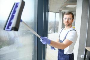 Male professional cleaning service worker in overalls cleans the windows and shop windows of a store with special equipment. photo