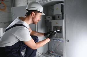Man, an electrical technician working in a switchboard with fuses. Installation and connection of electrical equipment. Professional with tools in hand. concept of complex work, space for text. photo