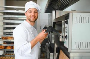 Portrait of handsome baker at the bakery with breads and oven on the background photo