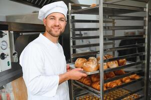 Male baker holding a tray of baked breads in bakery shop photo