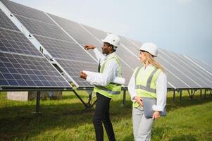 africano americano empresario y europeo hembra ingeniero hablando cerca solar paneles foto