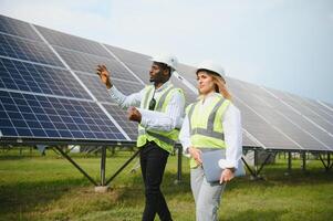 africano americano empresario y europeo hembra ingeniero hablando cerca solar paneles foto