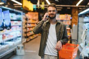 Quick text during shopping. Handsome young man holding mobile phone and smiling while standing in a food store photo