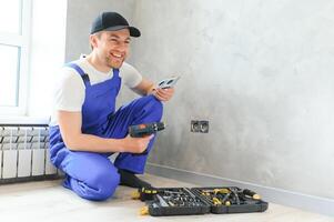 Confident professional electrician in uniform using screwdriver while replacing a socket in apartment after renovation work photo