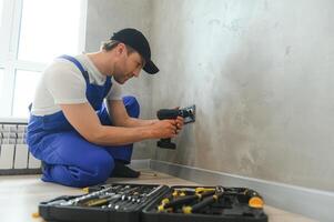 Smiling professional electrician in uniform replacing a socket in apartment after renovation work photo