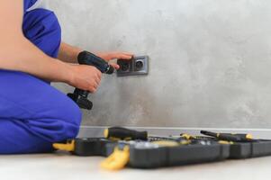 Smiling professional electrician in uniform replacing a socket in apartment after renovation work photo