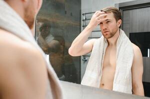 Young man looking in mirror after shaving at home photo
