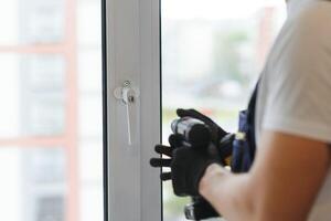 Workman in overalls installing or adjusting plastic windows in the living room at home photo