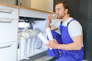 Plumber installs or change water filter. Replacement aqua filter. Repairman installing water filter cartridges in a kitchen. Installation of reverse osmosis water purification system. photo