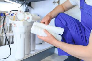 Plumber installs or change water filter. Replacement aqua filter. Repairman installing water filter cartridges in a kitchen. Installation of reverse osmosis water purification system. photo