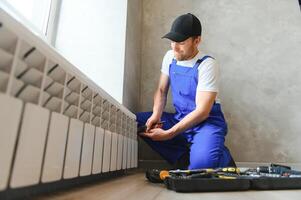 young man plumber checking radiator while installing heating system in apartment photo