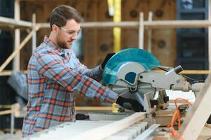 A carpenter works on woodworking the machine tool. Man collects furniture boxes. Saws furniture details with a circular saw. Process of sawing parts in parts. Against the background of the workshop. photo