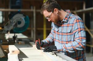 Professional carpenter using sawing machine for cutting wooden board at sawmill. Skilled cabinet maker working with electric circular saw at woodworking workshop. photo